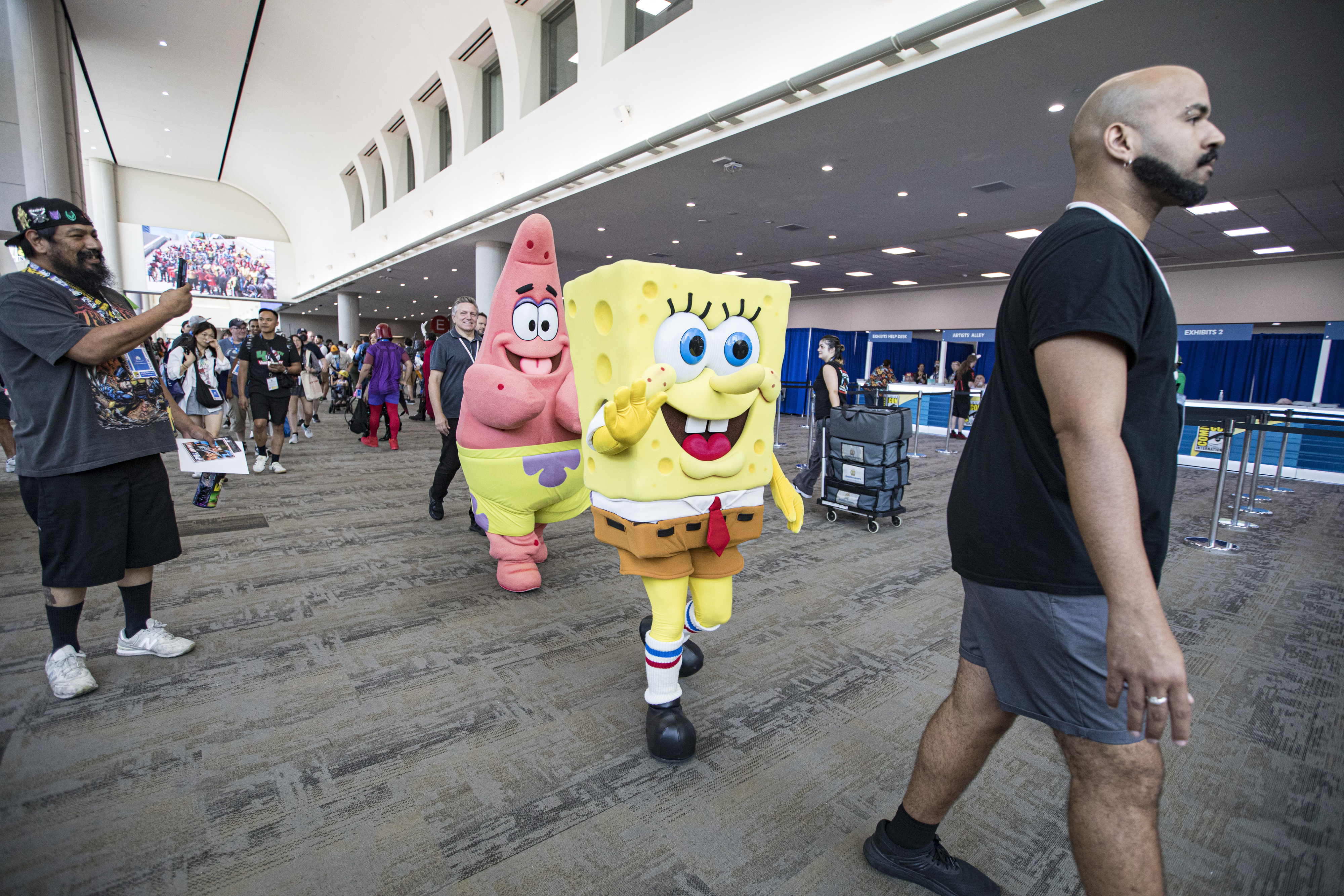 SpongeBob SquarePants and Patrick Star costumes being worn at a convention, with people in casual attire walking nearby