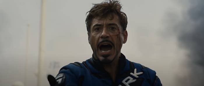 Robert Downey Jr. wearing a protective suit with &quot;STARK&quot; written on it, with a distressed expression and some dirt and cuts on his face