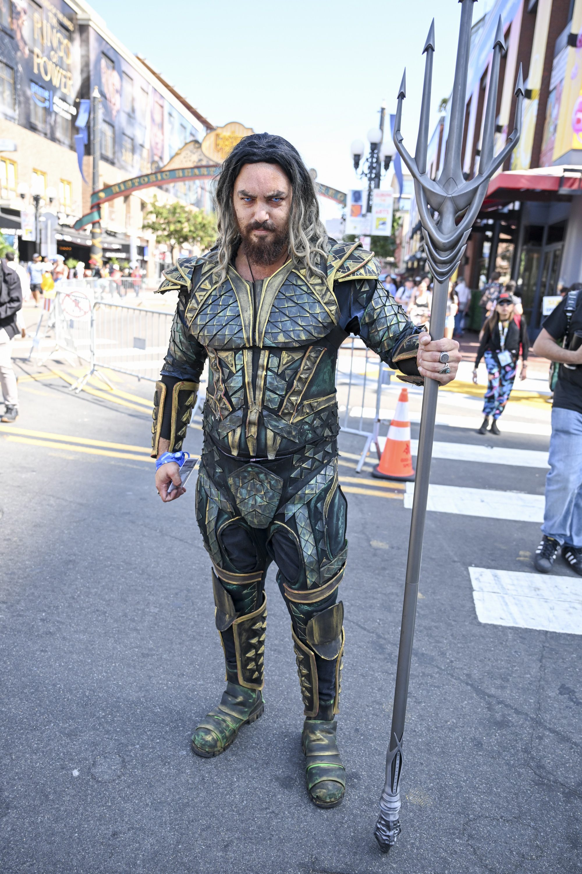 Jason Momoa in an Aquaman costume holding a trident on a city street