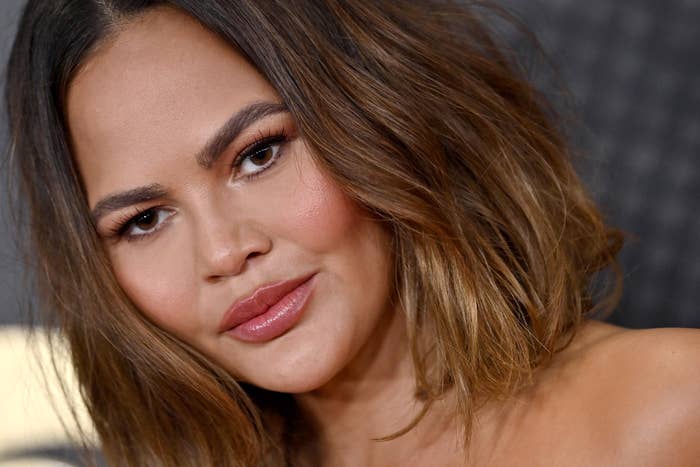 Close-up of Chrissy Teigen with shoulder-length wavy hair, light makeup, and a neutral expression, possibly at a celebrity event