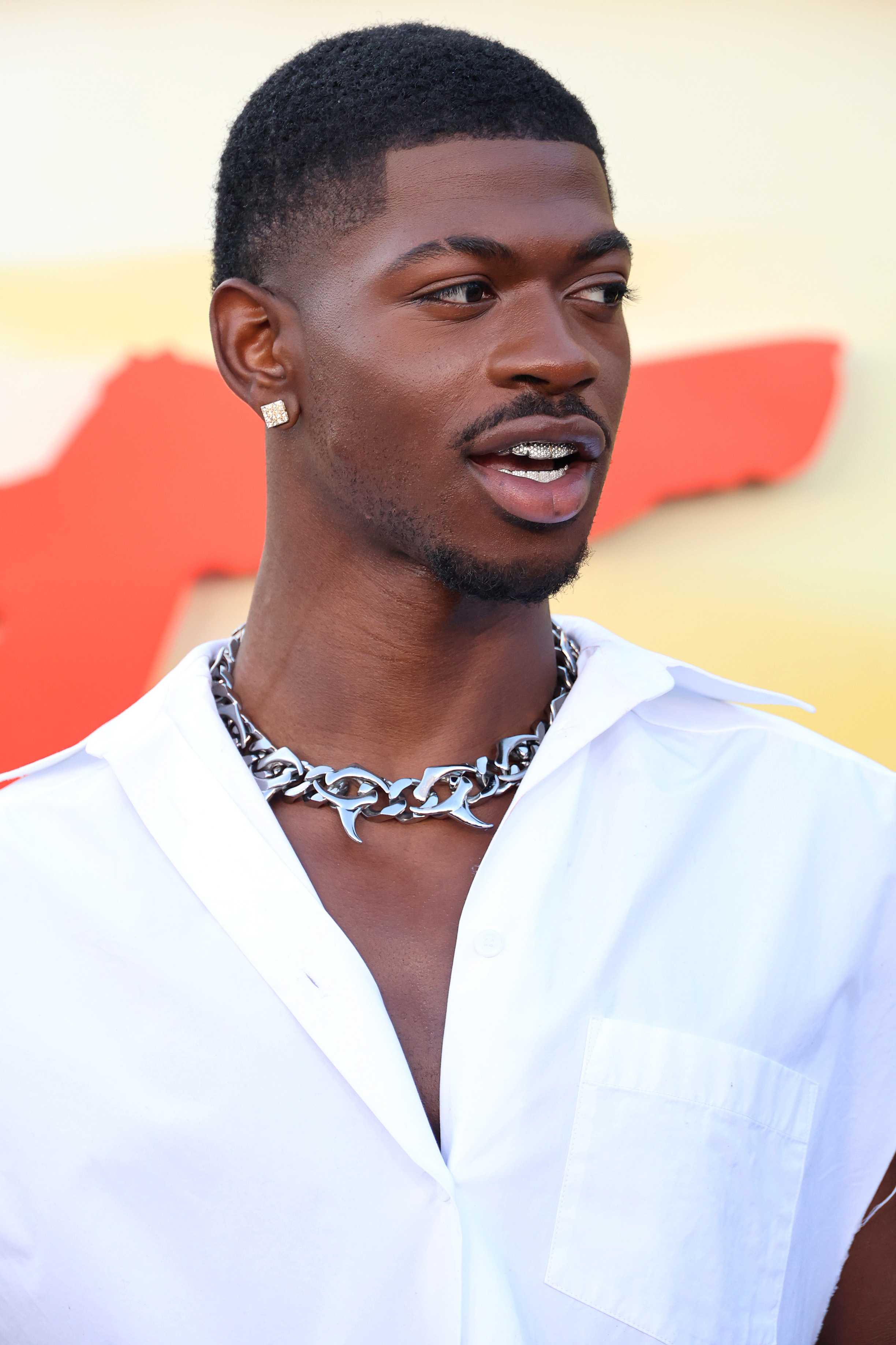 Lil Nas X at a red carpet event, wearing a white shirt with an open collar and a chunky chain necklace