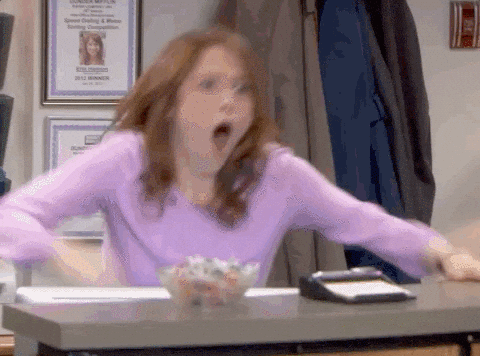 Woman in an office setting, in mid-motion with a surprised expression, by her desk. Plaques and jackets are on the wall behind her