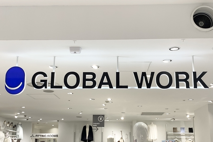 Storefront sign &ldquo;GLOBAL WORK&rdquo; inside a clothing store with mannequins, clothing racks, and fitting rooms in the background