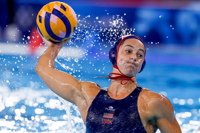 Team USA water polo player in mid-throw during a game, wearing a swim cap and suit
