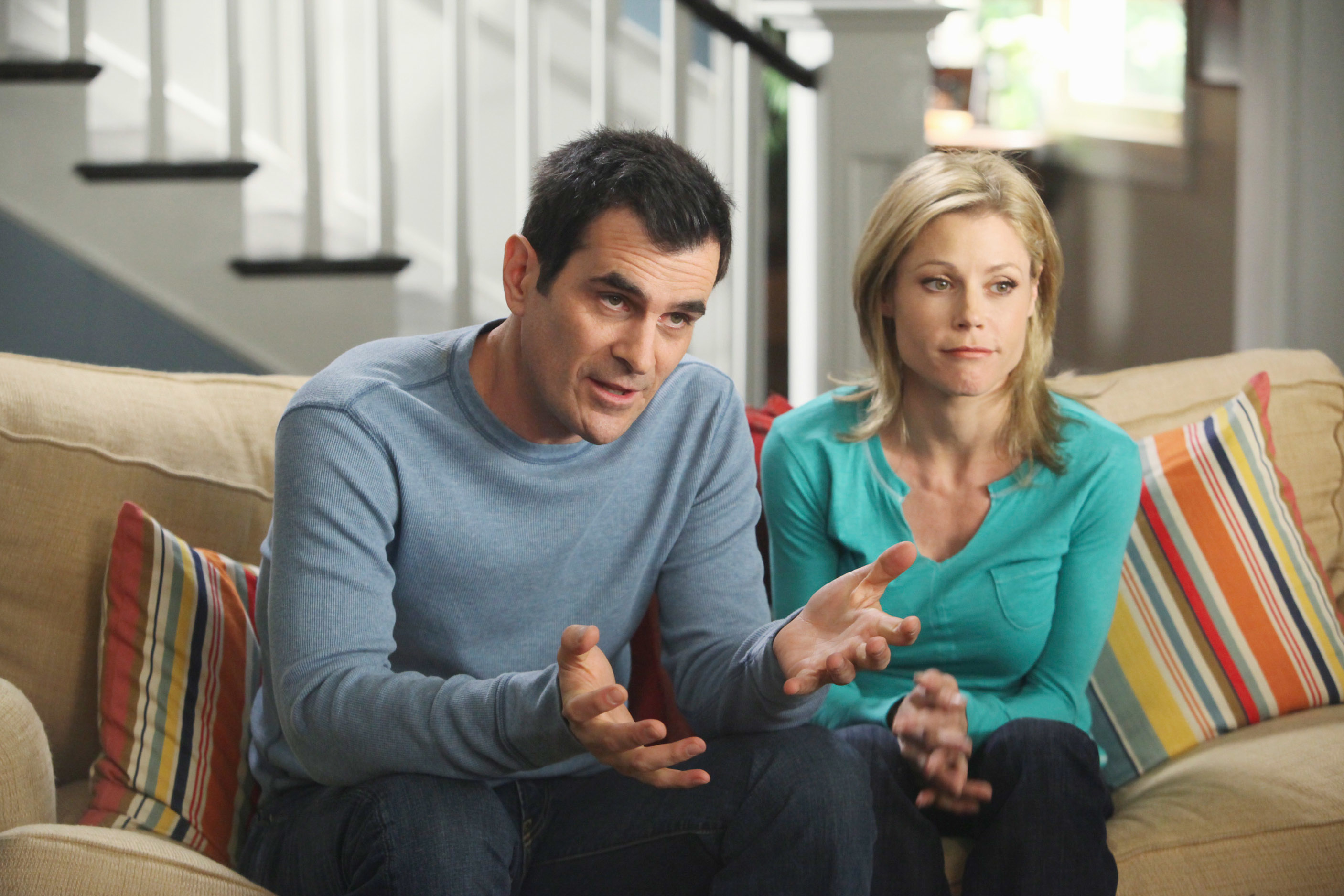 Ty Burrell and Julie Bowen sitting on a couch, wearing casual attire, in a scene from Modern Family