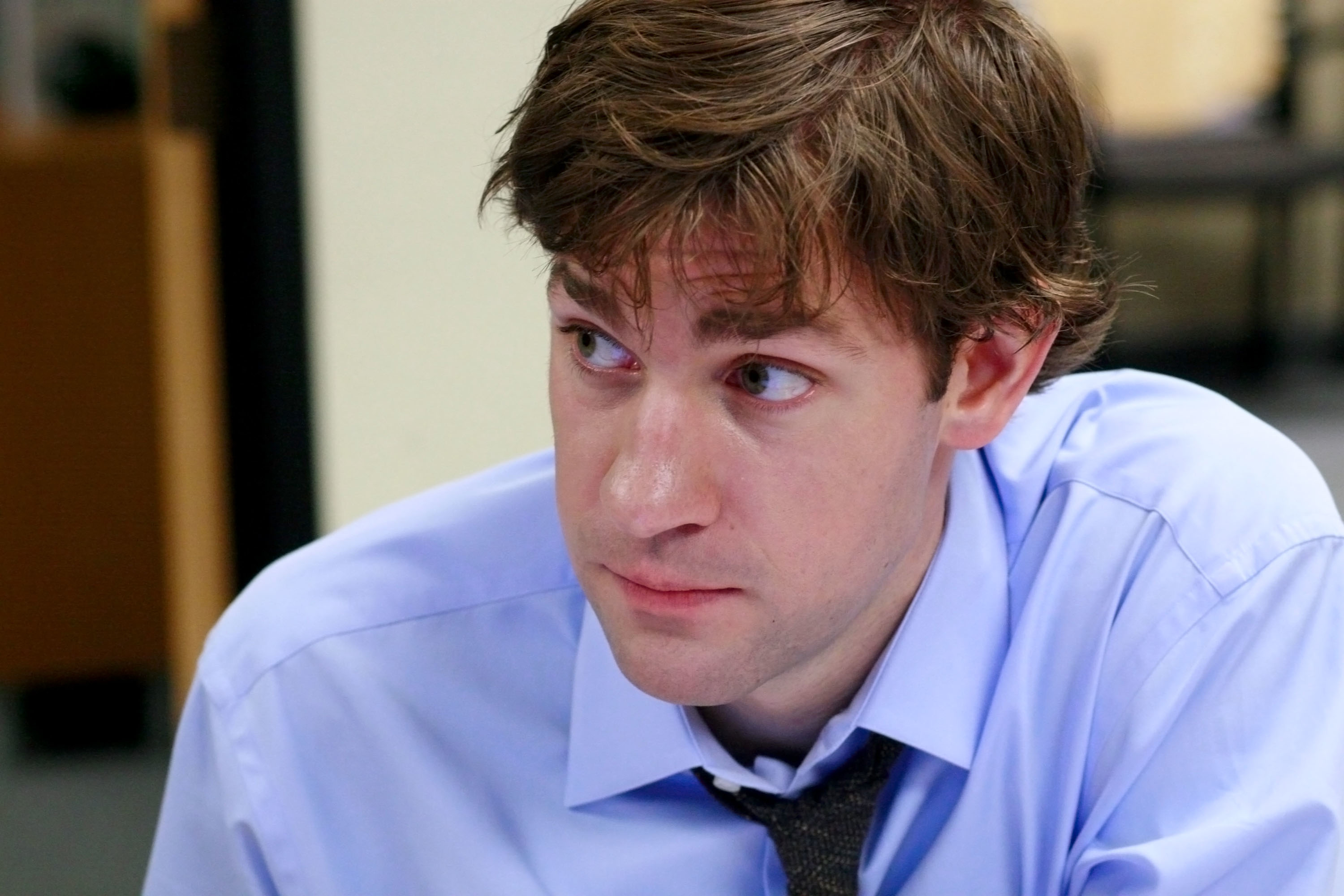John Krasinski, wearing a shirt and tie, looks to the side with a contemplative expression