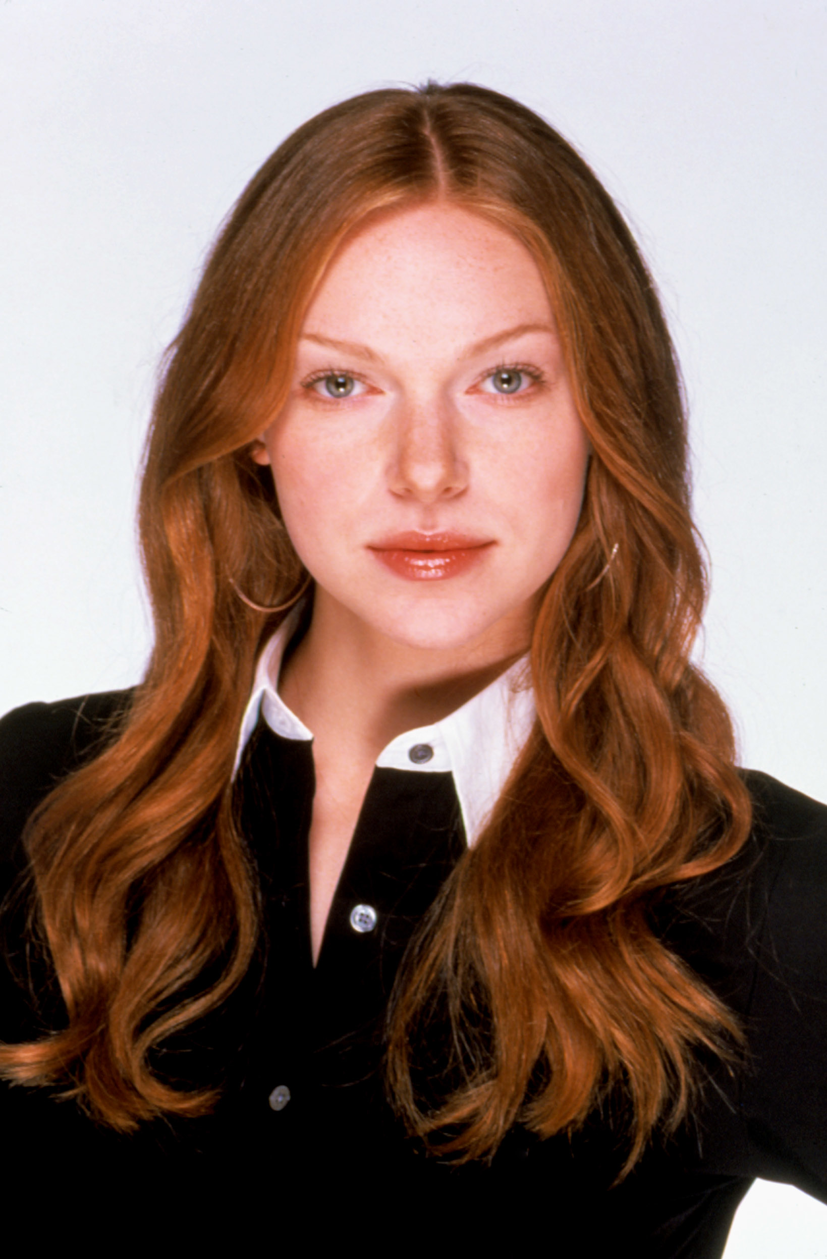 Laura Prepon poses for a headshot, wearing a dark top with a light collar and hoop earrings