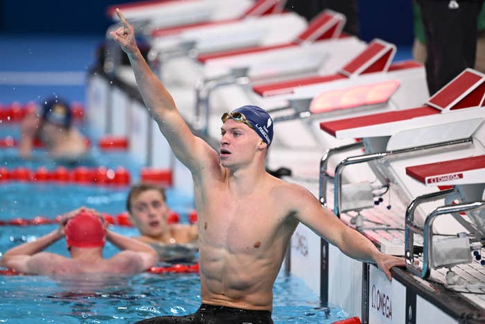 Swimmer raises arm in victory beside lane markers in a pool, two other swimmers in the background