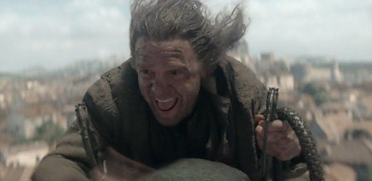 Persona con expresión alegre, cabello despeinado, y ropa desgastada, aparentemente en una escena de película o serie