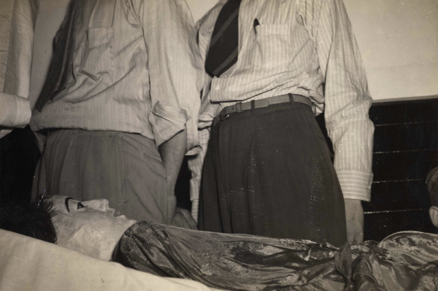 A deceased Albert Einstein lies on a stretcher, with three unidentified men standing around him in shirts and ties