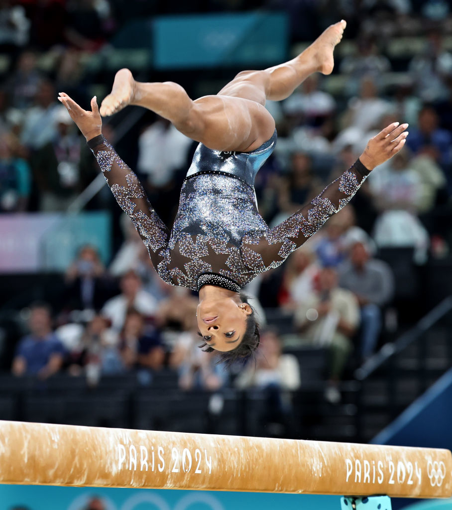 Simone Biles performs a flip on the balance beam at Paris 2024 Olympics, wearing a sparkling leotard with star patterns