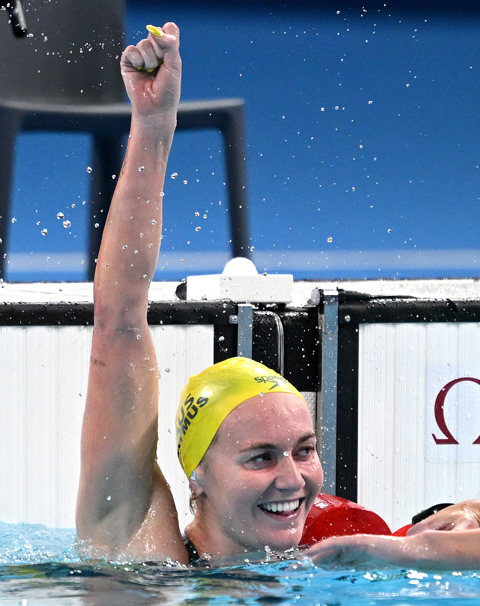 A female swimmer wearing a yellow swim cap and black swimsuit, smiling and raising her fist triumphantly in a pool