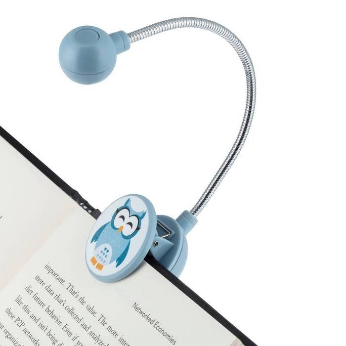 A flexible blue book light with an owl design, clipped onto an open book