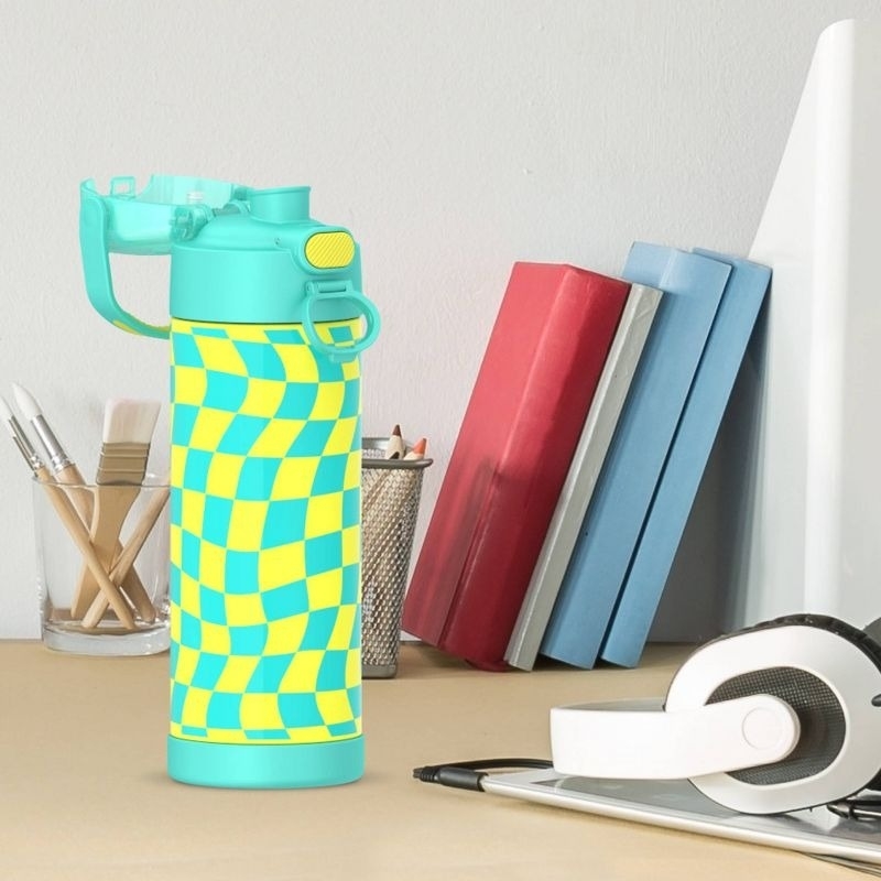 Turquoise water bottle with a yellow checkered pattern on a desk, surrounded by books, a computer, headphones, and brush holders