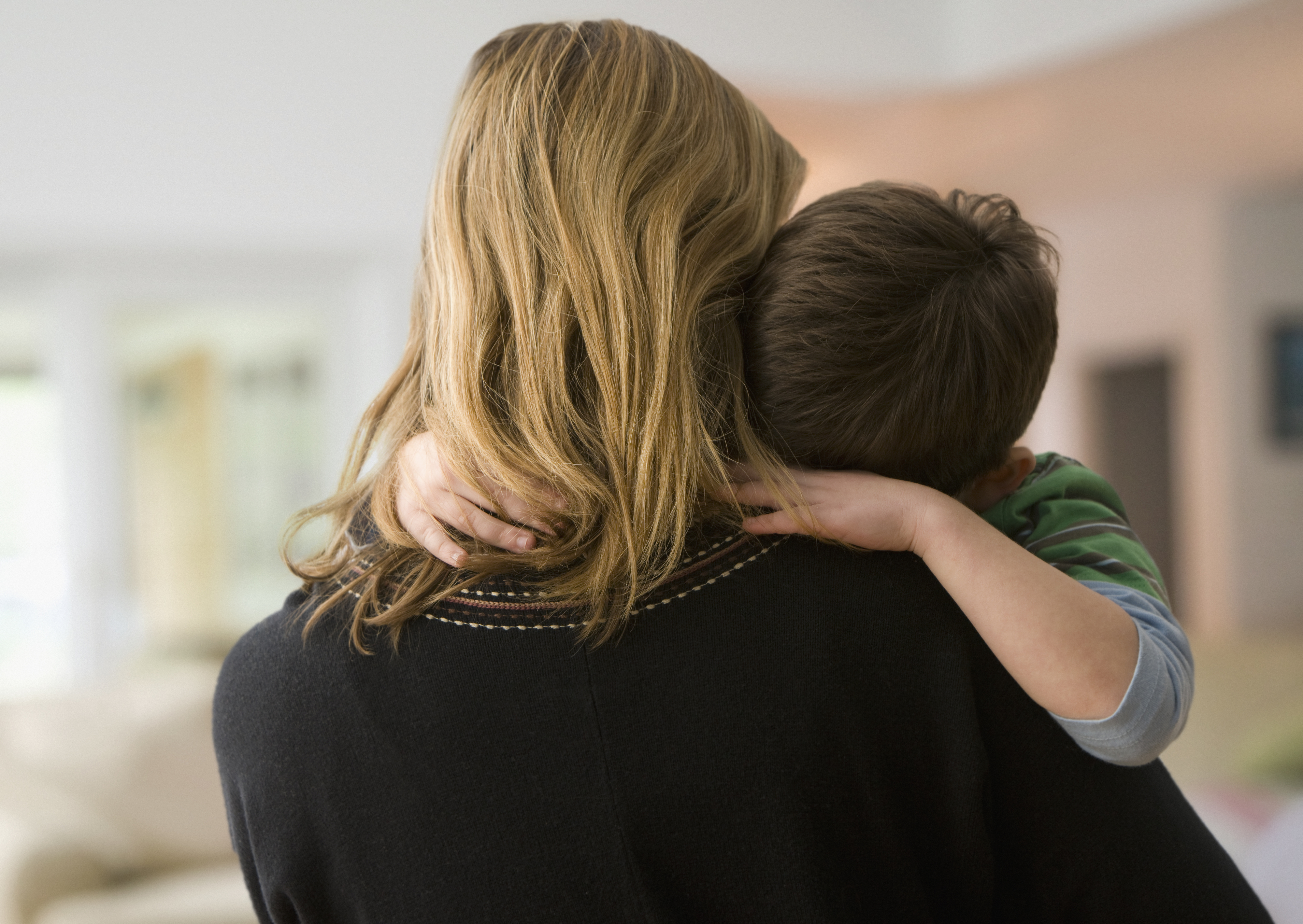 A parent embraces their child, who has their arms wrapped around the parent&#x27;s neck. The parent and child&#x27;s faces are not visible