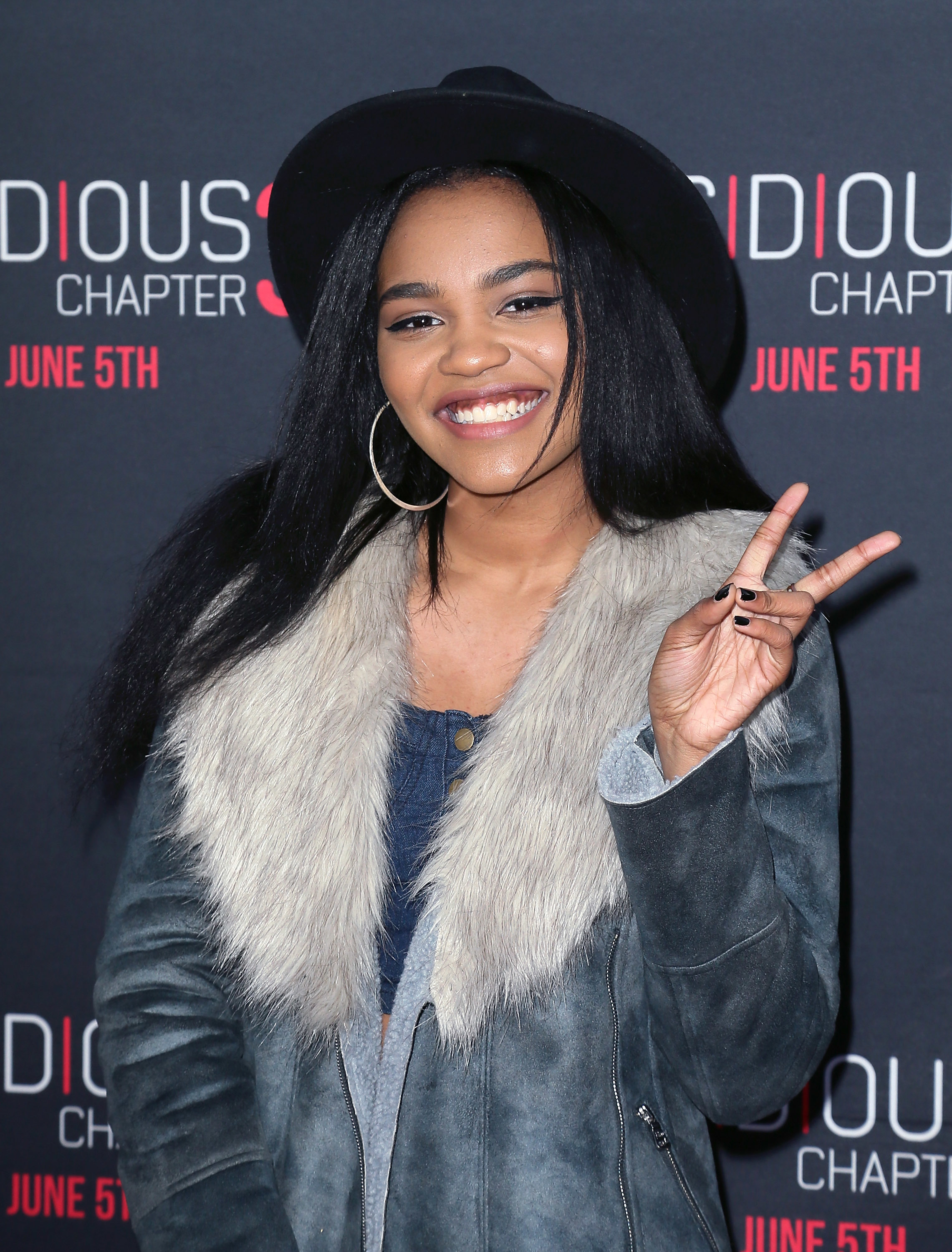 China Anne McClain poses in a faux fur-collared jacket and hat, smiling and flashing a peace sign at the "Insidious: Chapter 3" premiere
