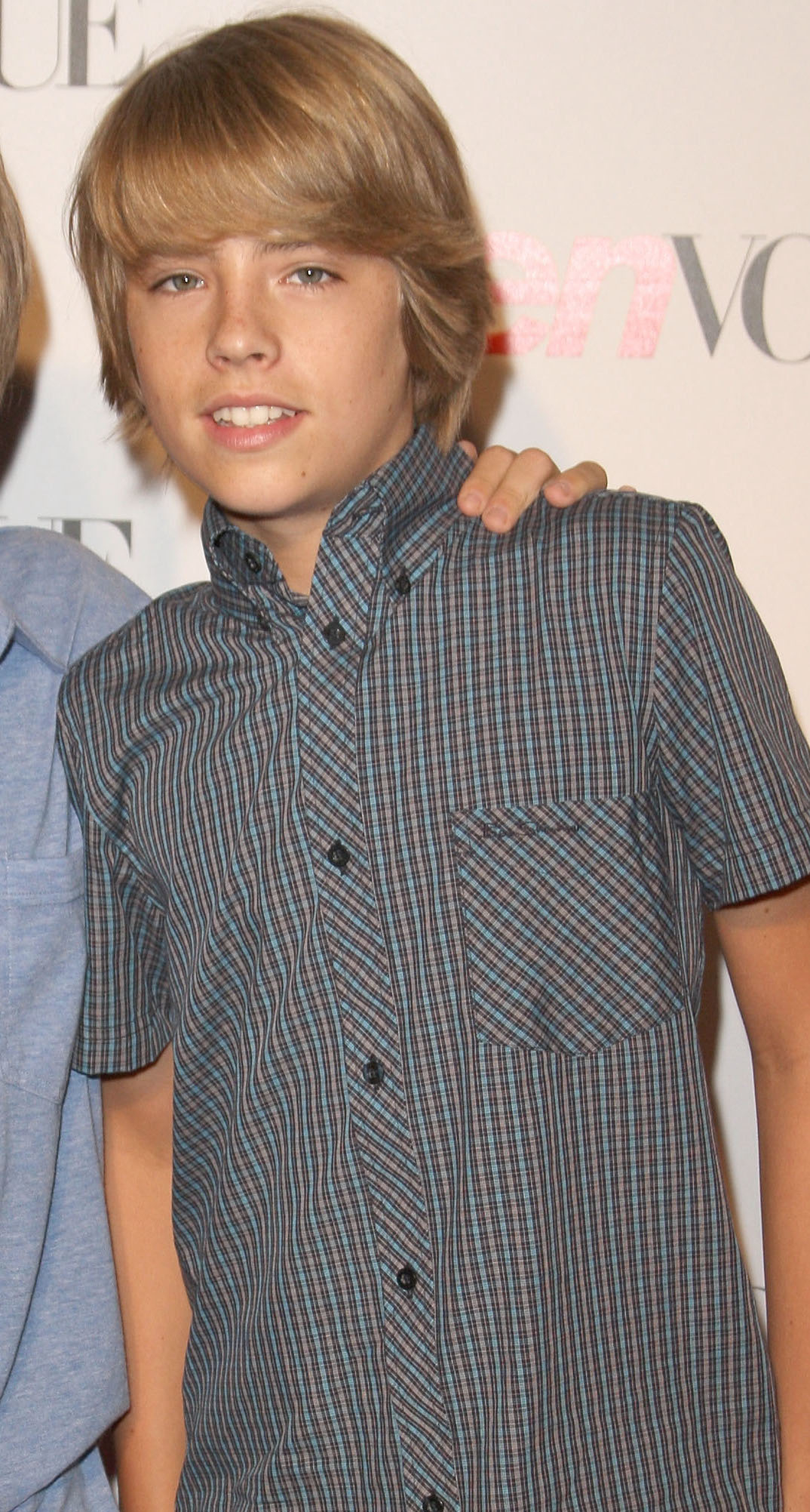 Dylan Sprouse at a red carpet event wearing a short-sleeved, button-up, patterned shirt