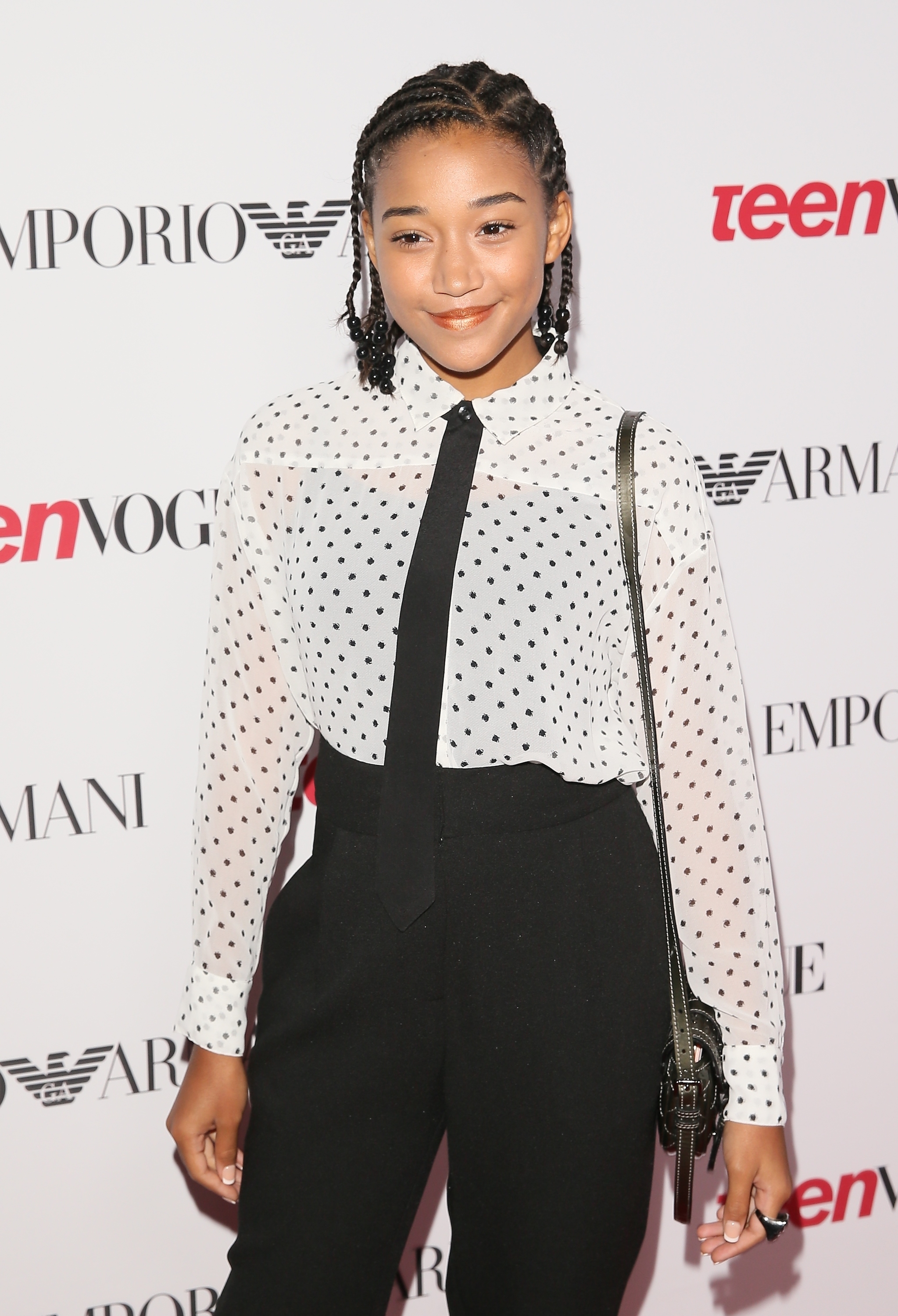 Amandla Stenberg on the red carpet in a white polka-dotted blouse and black pants at a Teen Vogue event