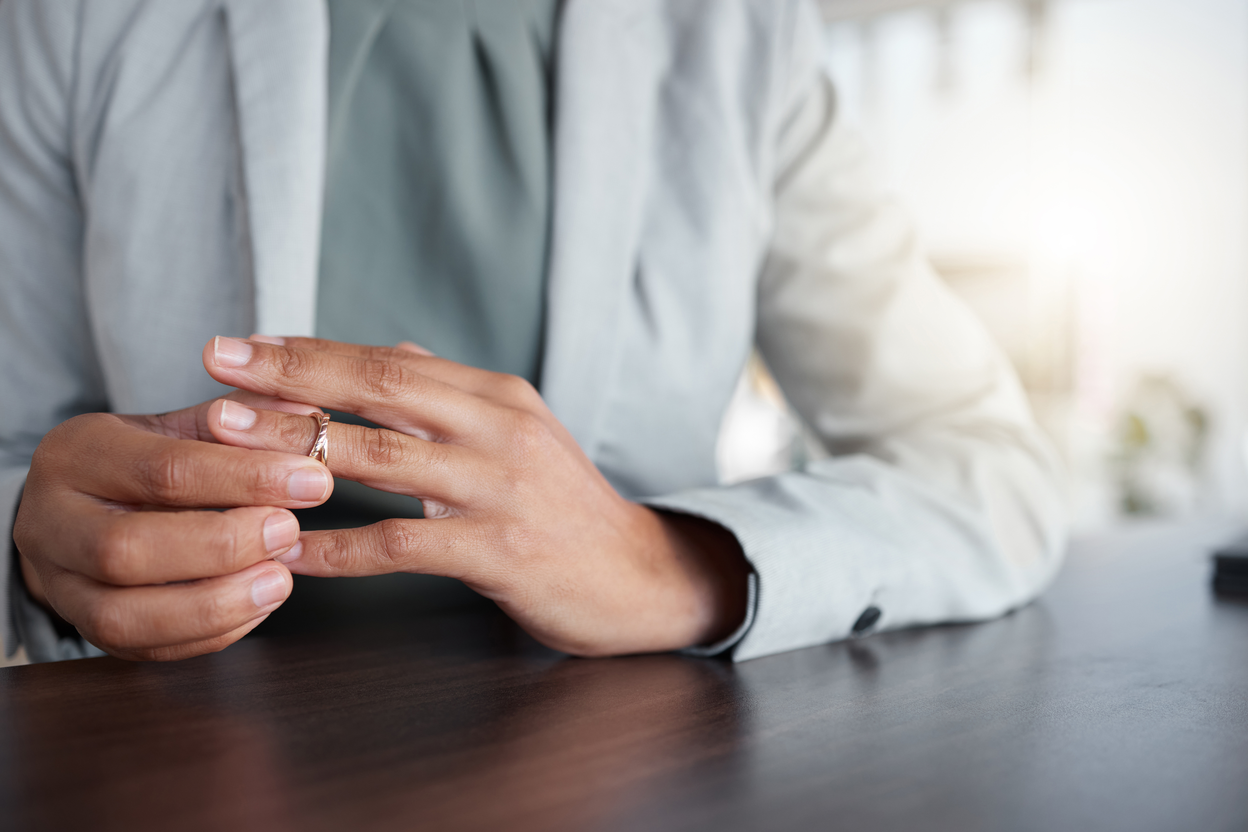 Close-up of a person at a desk, hands holding a ring, suggesting contemplation or removal of a wedding band