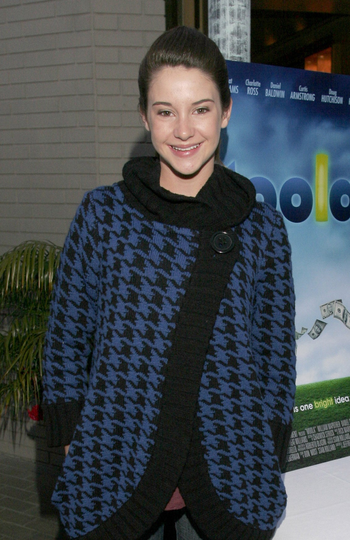 Leelee Sobieski at a movie premiere, wearing a patterned, oversized cardigan, skinny jeans, and black pointed-toe flats, standing beside a table