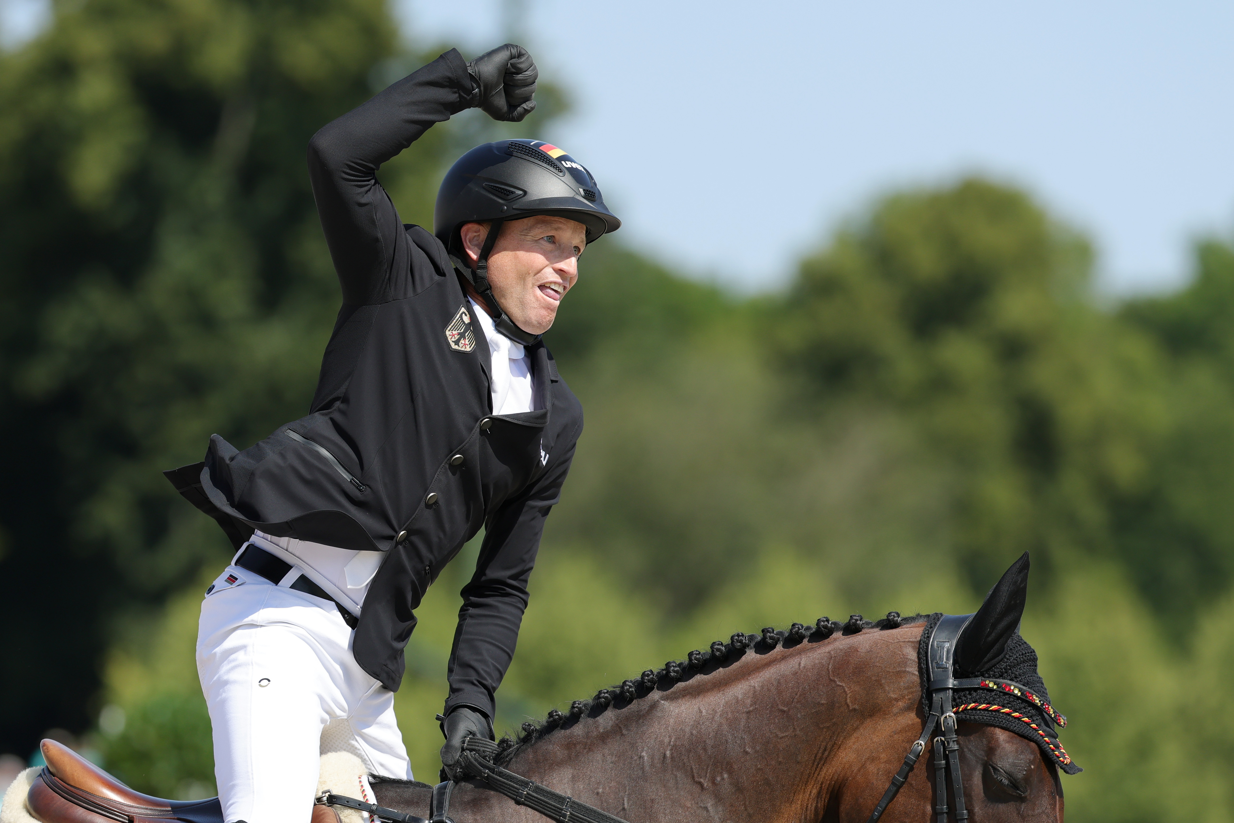 A person in equestrian attire and helmet raises a celebratory fist while riding a horse during a competition or event