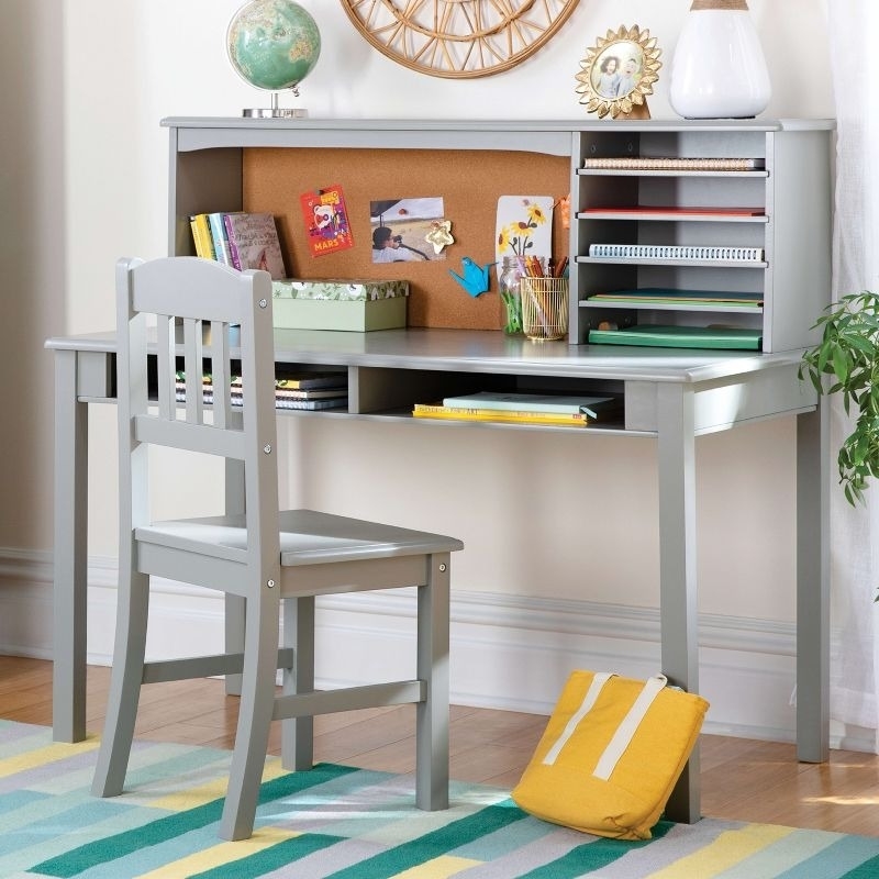 A grey wooden desk with a matching chair, featuring storage shelves, a corkboard with pinned notes, and a globe. A closed yellow bean bag lies nearby