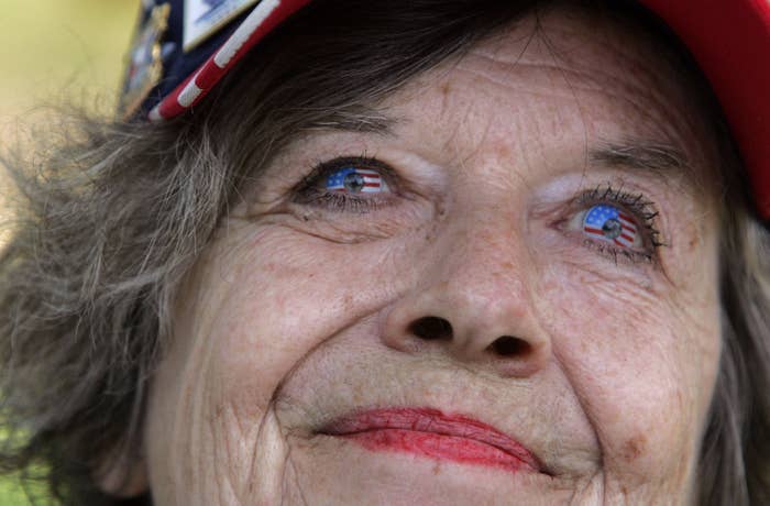 An elderly woman wearing a cap with a patriotic theme. Her eyelids are painted with American flags