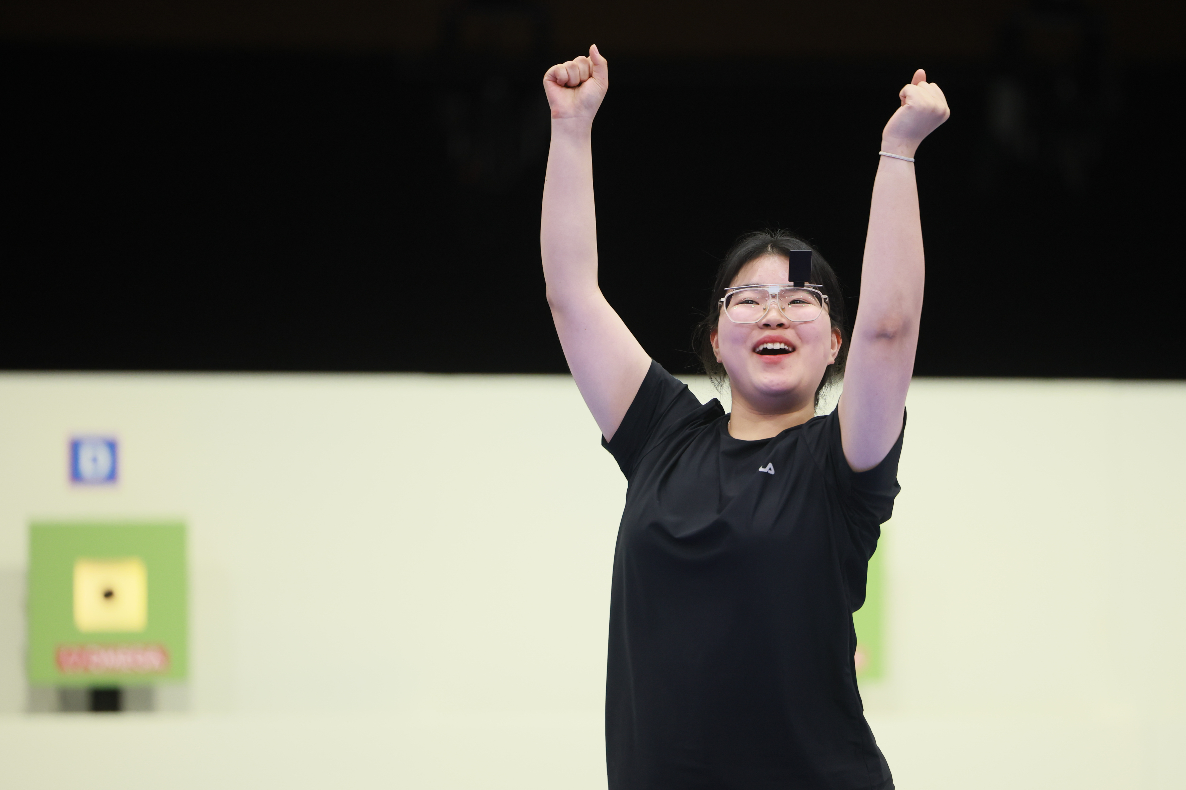 A woman in a black shirt celebrates with raised arms at a shooting range