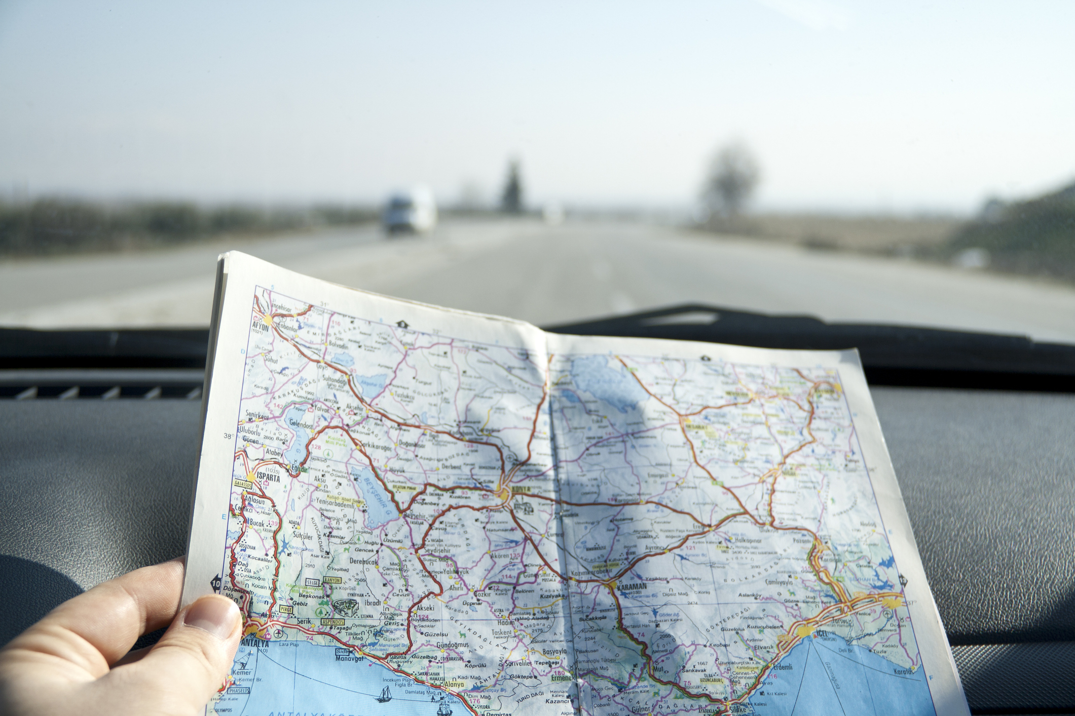 A person is holding a map inside a car as they drive on an open highway