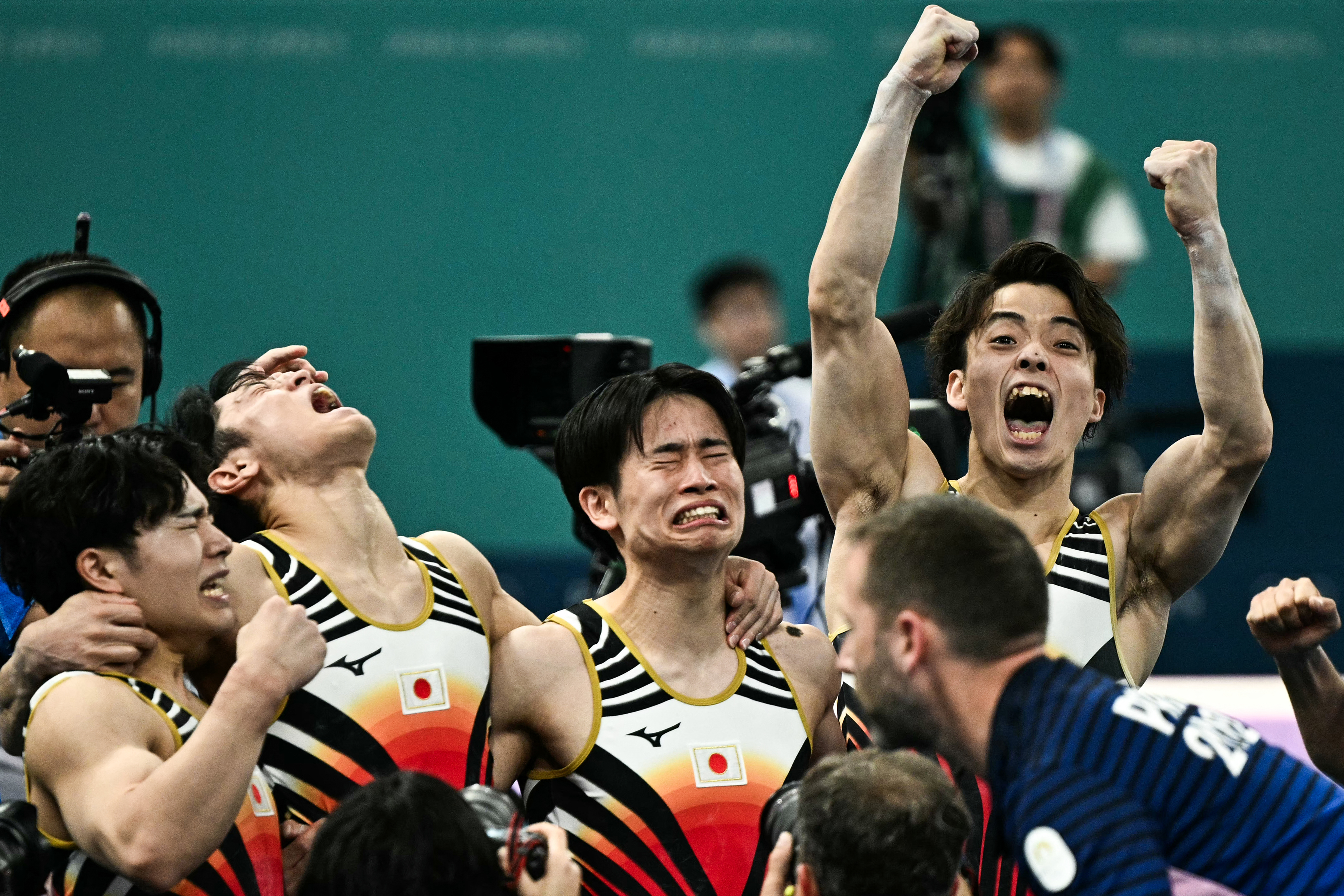 Daiki Hashimoto, Kohei Uchimura, Takeru Kitazono, and Kazuma Kaya celebrate with joy and emotion after a gymnastics competition. Japan flag on jerseys