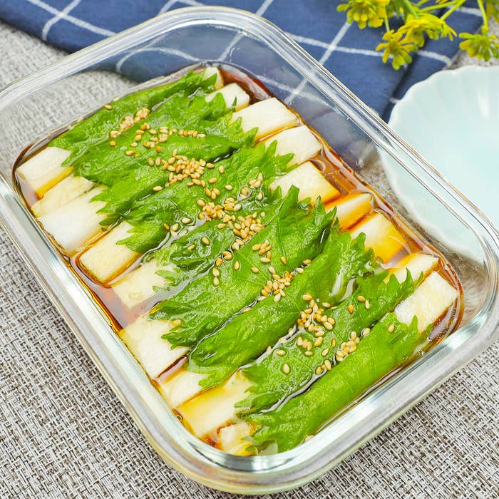 ガラス容器に盛り付けられた食材、葉物野菜と白い食材が醤油ベースのソースに浸っている。上にゴマが振りかけられている。