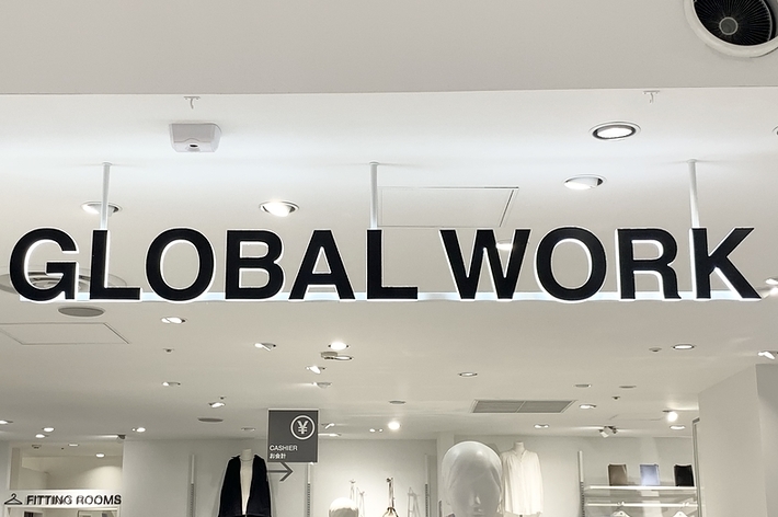 “Interior of a Global Work clothing store, featuring mannequins dressed in modern outfits and customers browsing. Signage for fitting rooms and a cash register is visible."