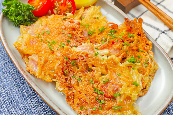 お好み焼きが皿に盛り付けられ、トマト、パセリ、レモンが添えられている。