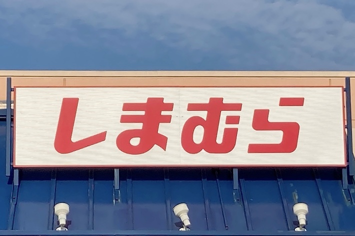 The image shows a storefront with a sign in Japanese that reads &ldquo;しまむら,&rdquo; which is a retail store name