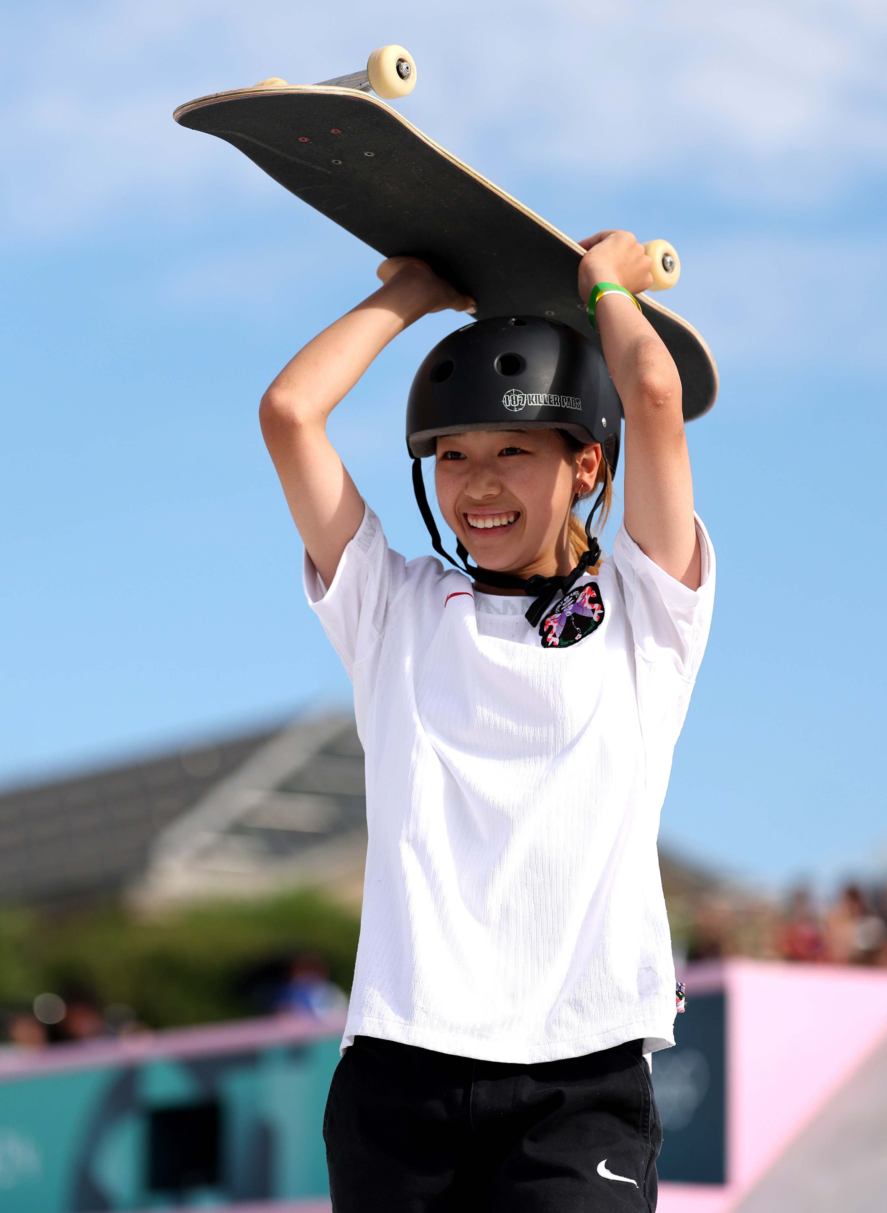 Young skateboarder holding a skateboard above head, celebrating at a skate park