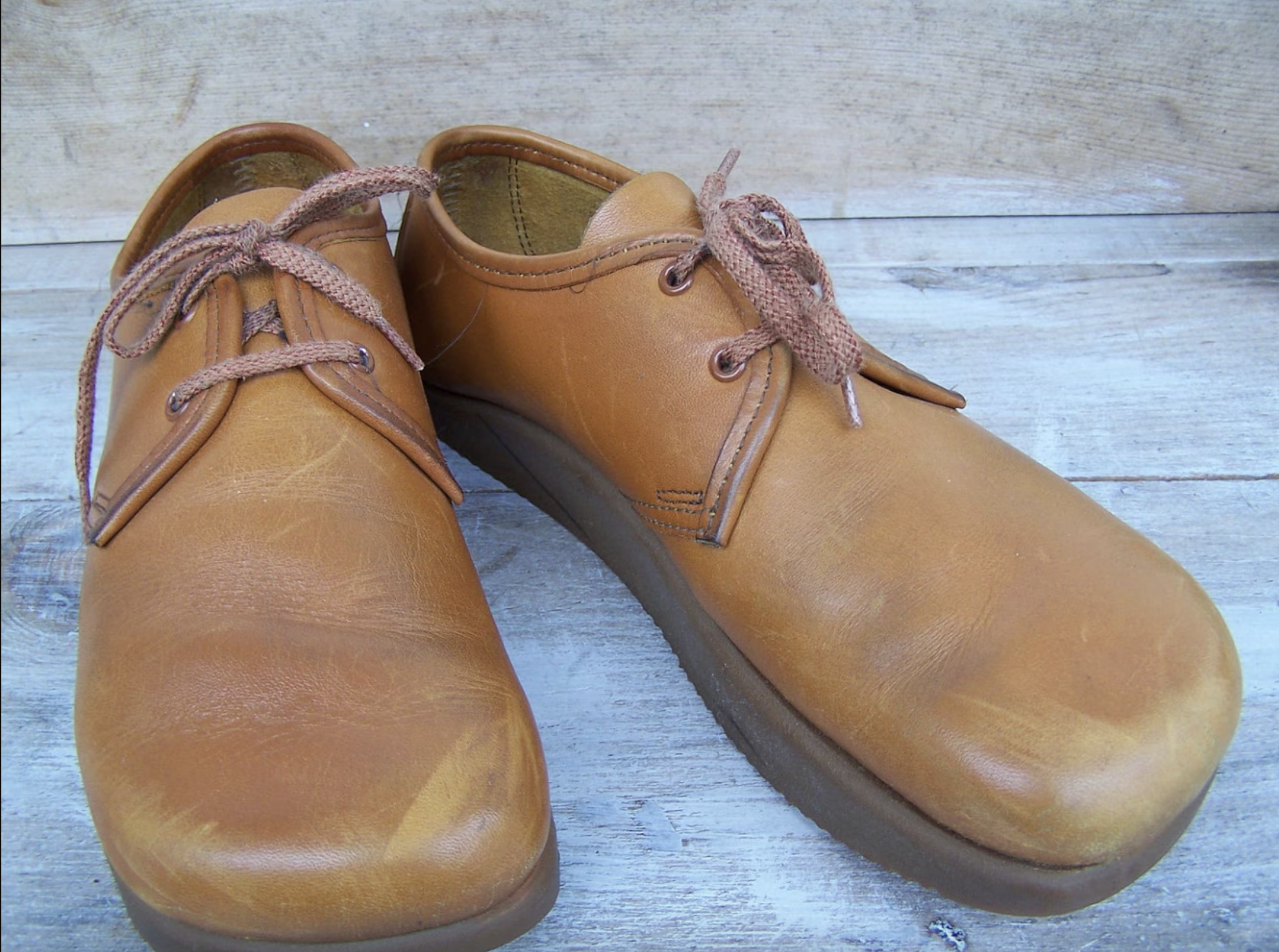 A pair of worn brown leather shoes with laces, placed on a wooden surface