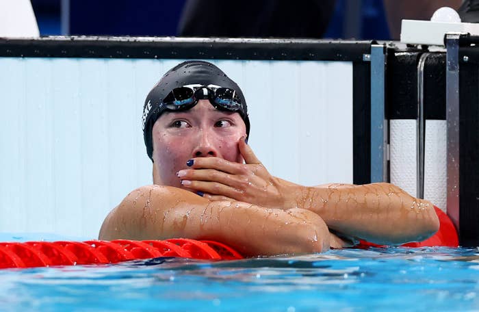 Swimmer rests at the pool edge, looking thoughtful, wearing a swim cap and goggles