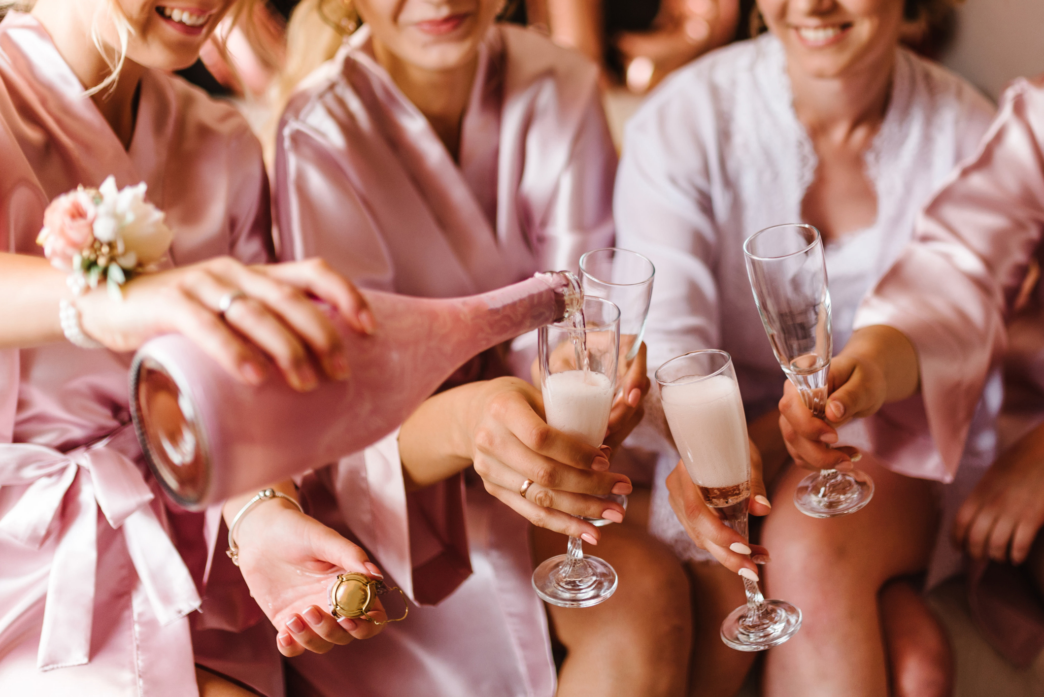 Women in satin robes are toasting with champagne flutes. One is pouring champagne. Faces are not shown