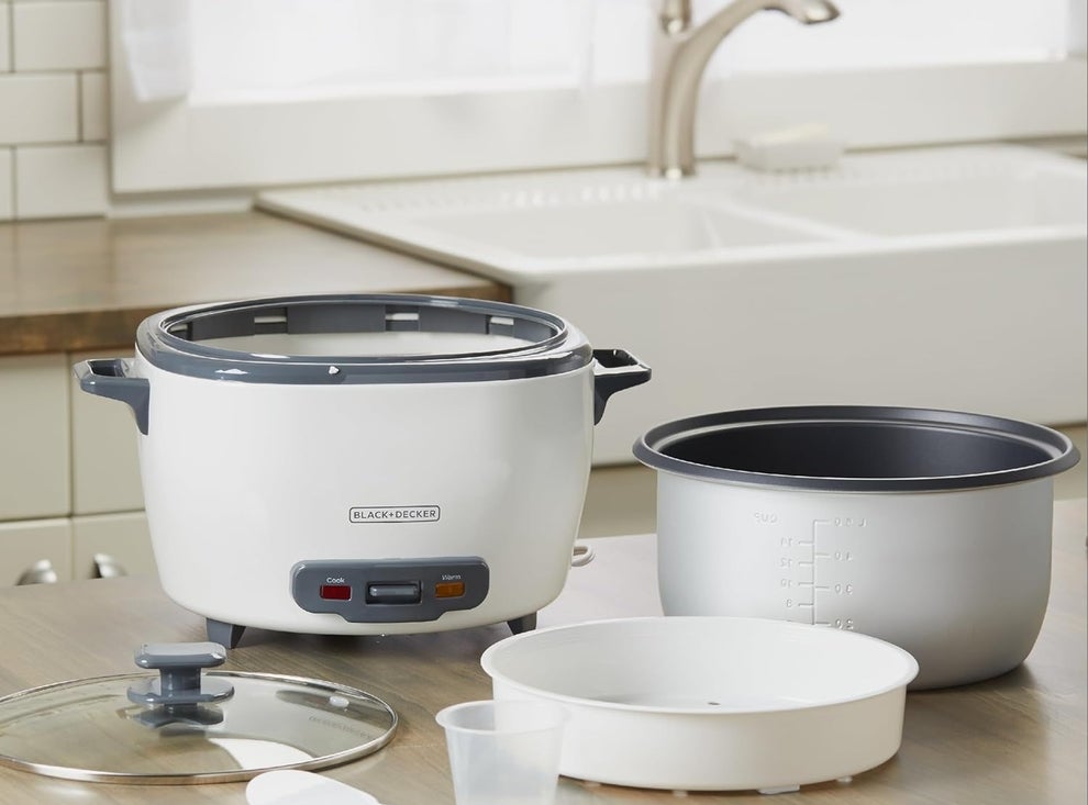 Black+Decker rice cooker with cooking base, bowl, steaming basket, glass lid, serving spoon, and rice measuring cup on a kitchen counter