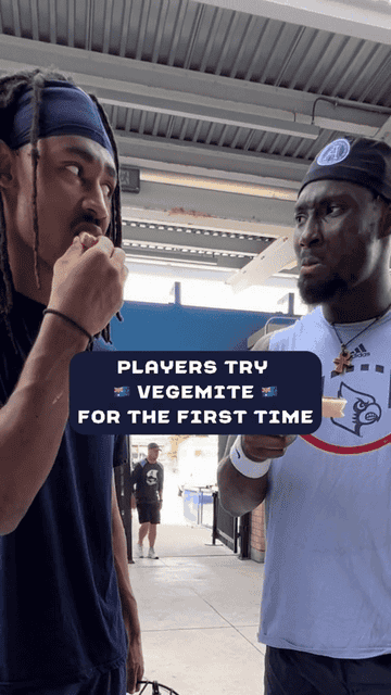 Two men, one eating and one holding bread, with text overlay: "Players Try Vegemite For The First Time."