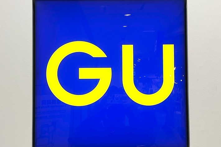 A square sign with the large yellow letters &ldquo;GU&rdquo; centered against a blue background