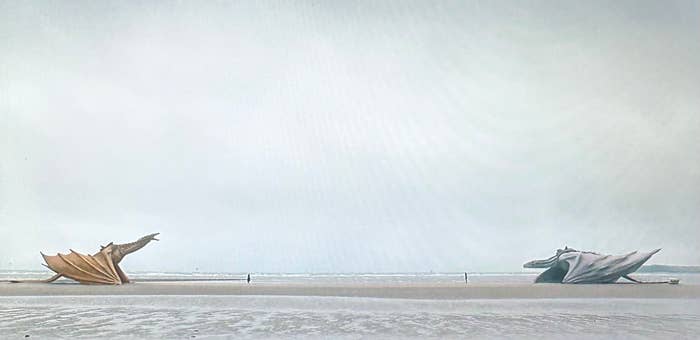 Escultura gigante de un dragón dorado junto a una escultura similar de un dragón gris en la orilla de una playa