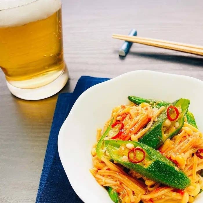 エリンギとオクラの和え物が白い器に盛られ、隣にビールのグラス、箸、ナプキンが置かれた食卓の写真。