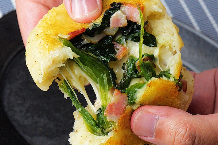 手で半分に割られた焼きたてのパンに、ほうれん草とベーコンが詰まっている。