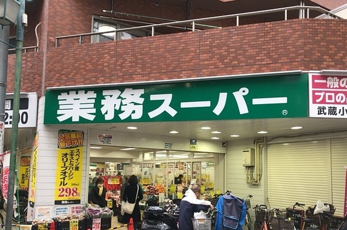 業務スーパーの外観。お客様が買い物中。店頭には特売商品が並んでいる。