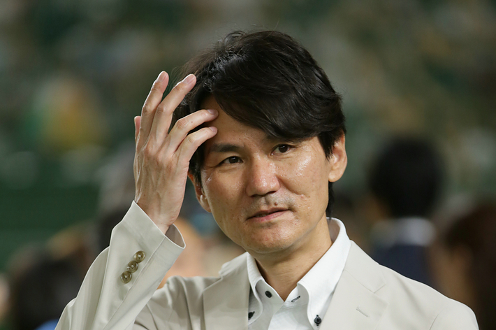 男性が明るい背景の前でカジュアルな白いジャケットとシャツを着て立っている。