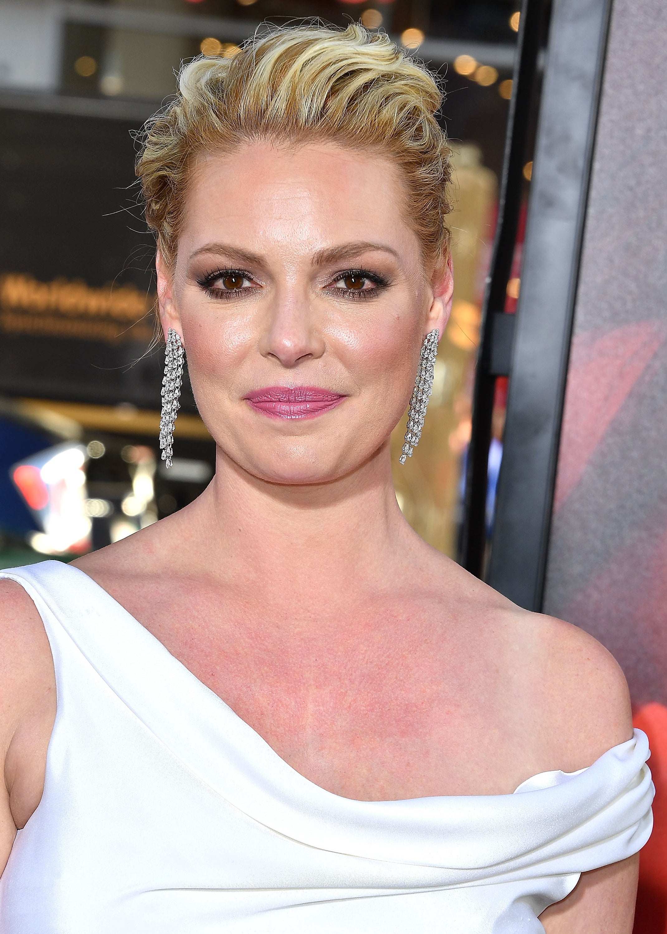 Katherine Heigl on the red carpet, wearing an elegant off-the-shoulder white dress and chandelier earrings