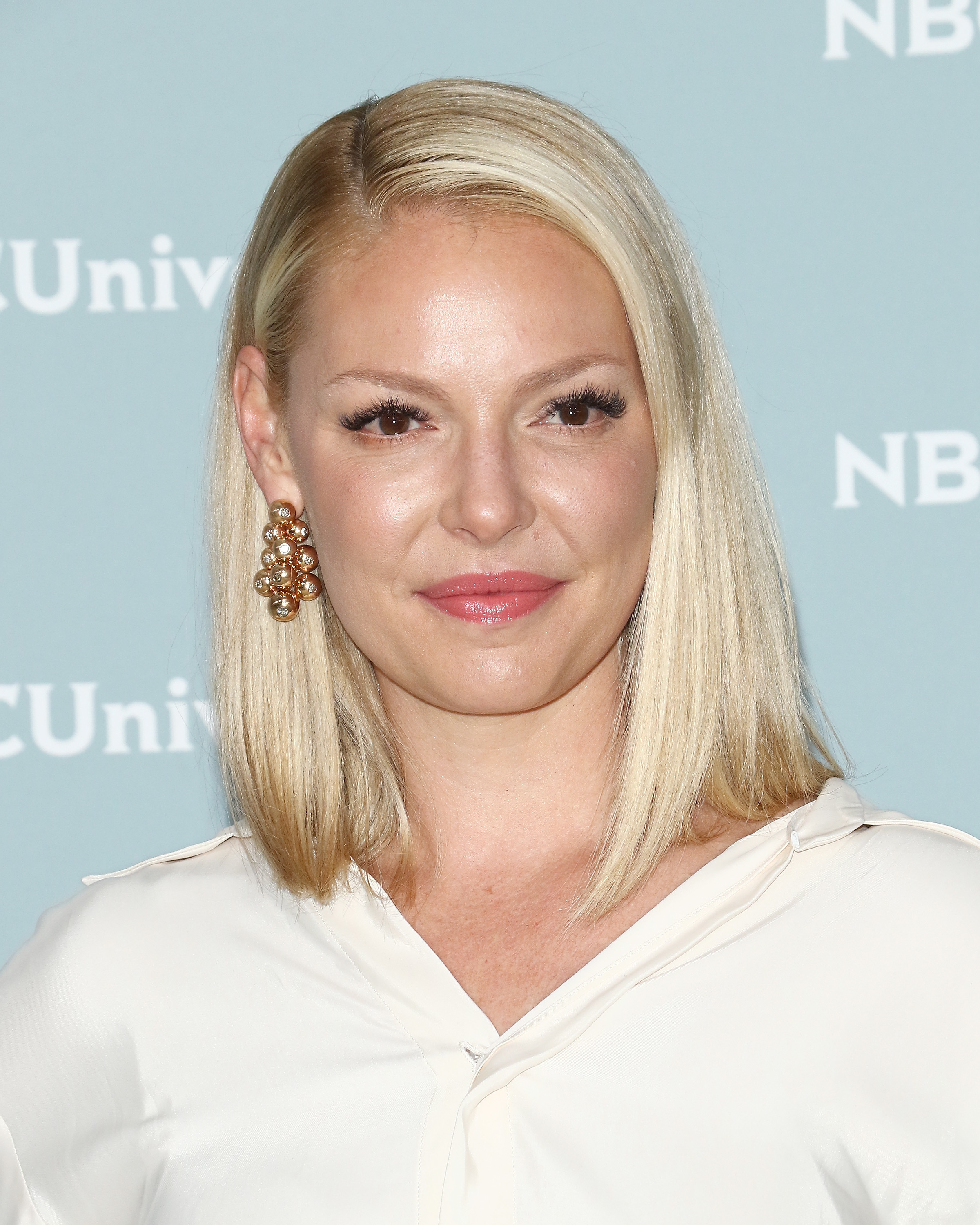 Katherine Heigl at an NBCUniversal event, wearing a simple white blouse and large, gold statement earrings