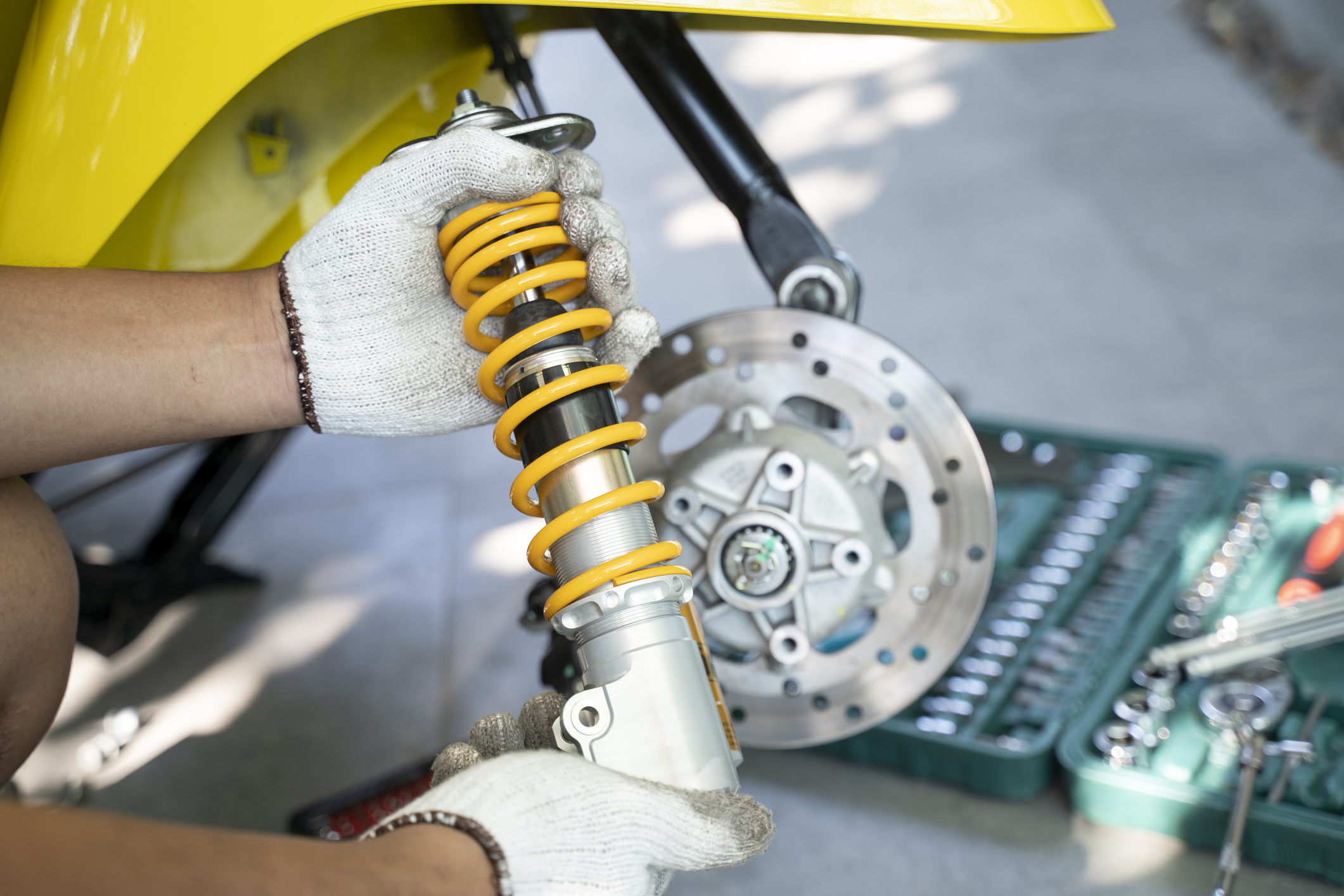 Person wearing gloves installs a motorcycle shock absorber beside a tool set and rear wheel