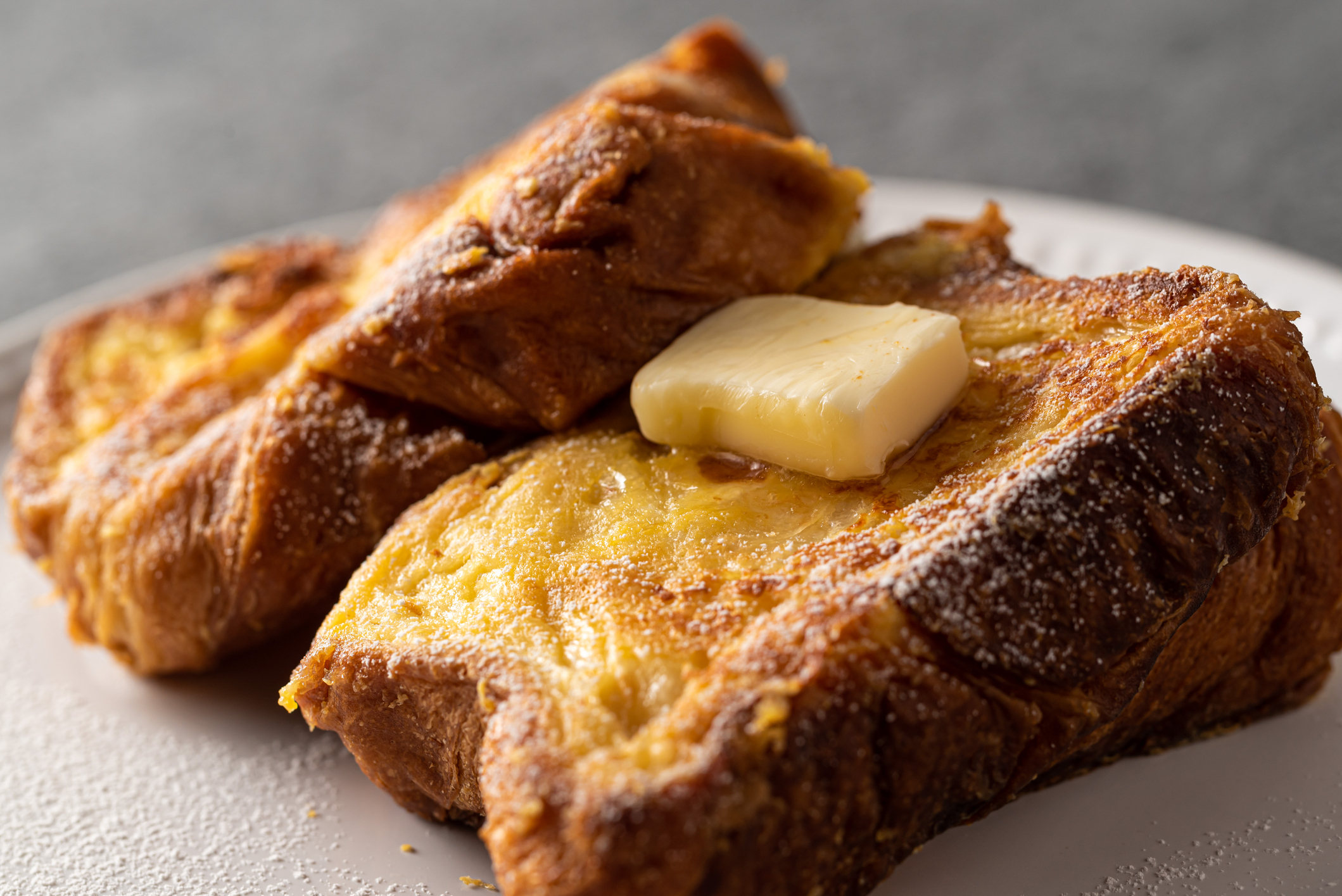 Close-up of three slices of French toast on a plate, with a pat of butter on top. The toast appears golden and crispy